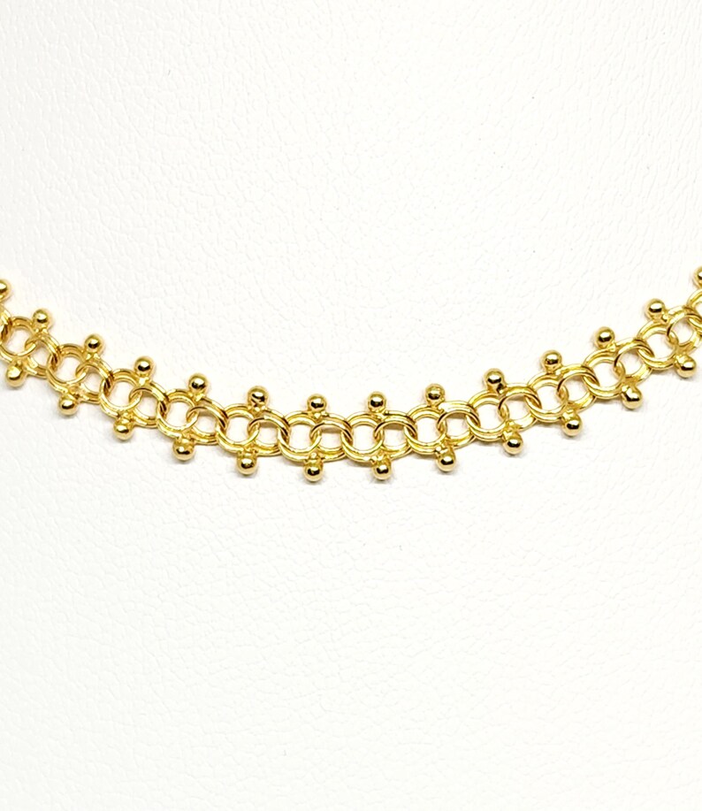 Pu&ograve; includere: Una collana a catena dorata con un design delicato che presenta piccole perle rotonde. La catena &egrave; composta da cerchi interconnessi con una perla in ogni punto in cui i cerchi si incontrano.