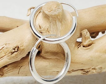 Puede incluir: Un par de pendientes de aro de plata pulida con un diseño circular y liso. Los pendientes están entrelazados, presentando una estructura de banda metálica simple y continua con una superficie reflectante que capta la luz.