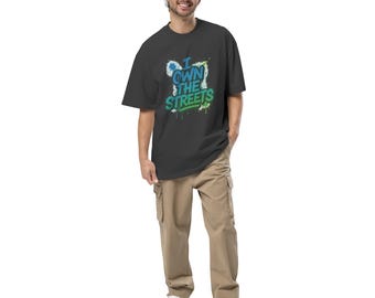 May include: A black oversized t-shirt with the text "I OWN THE STREETS" in blue and green graffiti-style lettering. The shirt is paired with khaki cargo pants and white sneakers. The person is smiling.