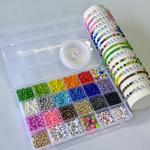 May include: A clear plastic organizer filled with colorful beads in various sizes and colors, alongside a spool of clear string. Several beaded bracelets with letter beads are displayed on a white cylinder, showcasing words and phrases.
