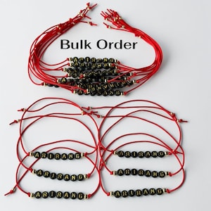 May include: A collection of red cord bracelets featuring black spherical beads with gold lettering that spells out ARIRANG. The bracelets are arranged in two groups, with the text Bulk Order displayed above the top cluster of bracelets.
