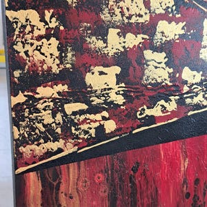 May include: Abstract painting on canvas with red, gold, and black paint. The painting has a textured surface and a geometric design.