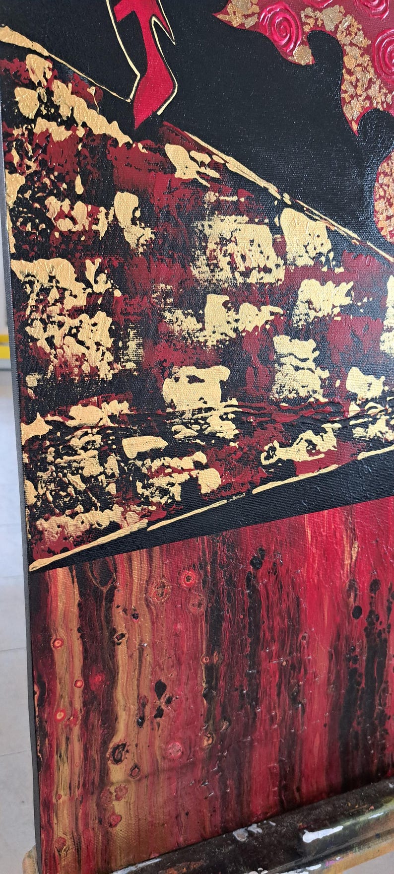 May include: Abstract painting on canvas with red, gold, and black paint. The painting has a textured surface and a geometric design.