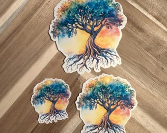 May include: Three tree-shaped stickers with a watercolor design. The trees have blue and rainbow-colored leaves, brown trunks, and exposed roots. The background features a yellow and orange gradient. The stickers are on a wooden surface.