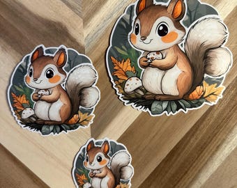 Puede incluir: Tres pegatinas de ardillas de dibujos animados en varios tamaños. Cada pegatina presenta una ardilla marrón y blanca sosteniendo una seta, sobre un fondo de hojas y follaje. Las ardillas tienen mejillas naranjas y colas esponjosas.