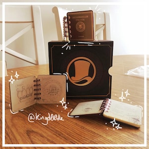 May include: A collection of miniature notebooks and a box, all with a vintage aesthetic. The notebooks have spiral bindings and feature sketches and handwritten notes. The box is dark with a gold emblem. One notebook is labeled "Gresshenller College, London."