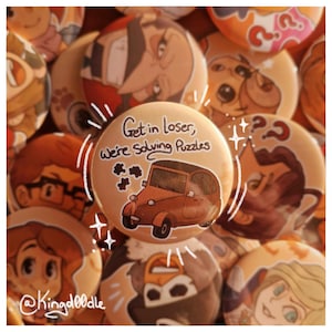 Könnte beinhalten: Eine Sammlung runder, hellbrauner Buttons mit Cartoon-Illustrationen. Ein Button zeigt ein braunes Auto und den Text "Get in loser, we're solving puzzles." Andere Buttons haben verschiedene Charakterdesigns. Der Name des Künstlers, @Kingdoodle, befindet sich unten links.