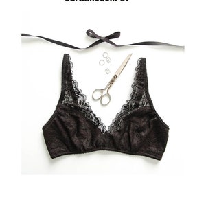 Può includere: Reggiseno in pizzo nero con scollatura a V profonda. Il reggiseno è su una superficie bianca con un paio di forbici e alcuni piccoli anelli metallici. Il testo "Cartammodelli dv" e "Taglia da XS a XL" è visibile.