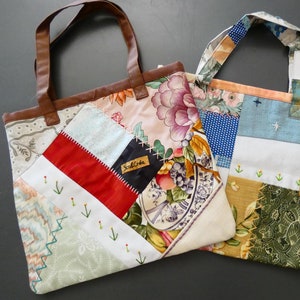Peut inclure: Deux sacs cabas en patchwork avec des anses en cuir marron. Le sac à gauche a un motif floral et le sac à droite a un design patchwork bleu, vert et rouge. Les deux sacs ont une petite étiquette qui dit "Scall Crafts".