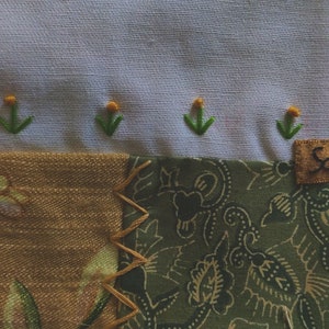 Pode incluir: Uma colcha de retalhos com uma variedade de tecidos, incluindo vichy azul e branco, flores marrons e brancas e paisley verde. A colcha &eacute; decorada com flores amarelas bordadas e caules verdes. A colcha tem uma etiqueta que diz "Scroll Creek".