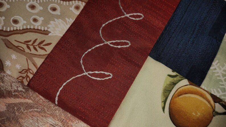 Pode incluir: Um close-up de um cobertor de retalhos com diferentes tecidos e padr&otilde;es. O cobertor &eacute; feito de uma variedade de cores, incluindo marrom, bege, vermelho, azul e verde. O cobertor tem um design bordado branco no tecido vermelho.