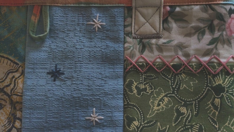 Pode incluir: Uma bolsa tote de tecido azul com um design de patchwork. A bolsa tem uma al&ccedil;a de couro marrom e um detalhe costurado rosa. O tecido &eacute; texturizado e tem um padr&atilde;o de estrelas.