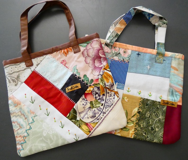 Pode incluir: Duas bolsas tote de patchwork com al&ccedil;as de couro marrom. A bolsa &agrave; esquerda tem um padr&atilde;o floral e a bolsa &agrave; direita tem um design de patchwork azul, verde e vermelho. Ambas as bolsas t&ecirc;m um pequeno r&oacute;tulo que diz "Scall Crafts".