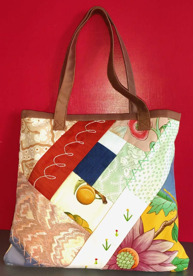 Pode incluir: Uma bolsa tote de patchwork com al&ccedil;as de couro marrom. A bolsa &eacute; feita de diferentes tecidos com padr&otilde;es florais e geom&eacute;tricos em tons de vermelho, azul, verde, amarelo e branco.