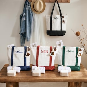 Könnte beinhalten: Weiße Canvas-Tragetaschen mit farbigen Akzenten und personalisierten Namen. Jede Tasche hat eine passende herzförmige Sonnenbrille. Die Taschen werden auf einem Holztisch präsentiert.