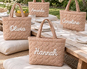 Peut inclure: Quatre sacs fourre-tout matelassés en tissu vichy marron et blanc. Chaque sac possède deux anses et un prénom brodé en blanc sur le devant, indiquant Olivia, Amanda, Caroline et Hannah. Les sacs présentent un motif à surpiqûres en losange.
