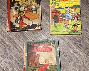 May include: Three vintage "Big Little Books" are displayed. The books feature colorful illustrations of classic cartoon characters. One book features Mickey Mouse as a pilot, another features The Flintstones, and the third features Little Orphan Annie.