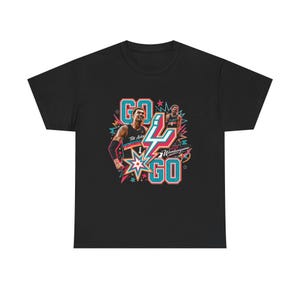 May include: Black t-shirt featuring a colorful graphic design with the words "GO" and "4 GO" in teal and white, along with images of basketball players. The design includes starbursts and the text "The Alamo" and "Wembanyama".