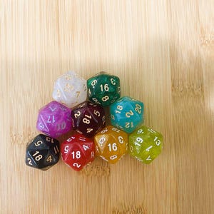 May include: A collection of ten polyhedral dice in various colors, including white, green, purple, red, and yellow. Each die features white or gold numbering. The dice are arranged on a light brown wooden surface.