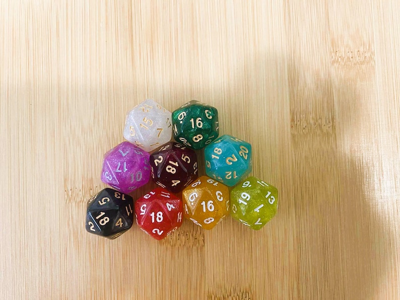 May include: A collection of ten polyhedral dice in various colors, including white, green, purple, red, and yellow. Each die features white or gold numbering. The dice are arranged on a light brown wooden surface.