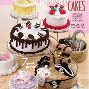 May include: Seven crocheted cake-shaped storage boxes with various designs, including a yellow cake with a cherry on top, a chocolate cake with chocolate frosting and Oreo cookies, a white cake with strawberries, a pirate treasure chest, and a purple cake with a crown. The text "Treasure Cakes" is written in large letters at the top of the image. The text "7 great projects" is written in smaller letters below the cakes.