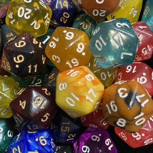 May include: A collection of colorful polyhedral dice in various shapes and sizes. The dice are made of translucent and opaque materials in shades of yellow, orange, blue, purple, and green. Each die features white or gold numbering.