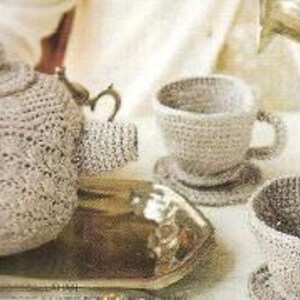 Peut inclure: Un ensemble de thé en crochet composé d'une théière, deux tasses et deux soucoupes. L'ensemble est de couleur beige clair.