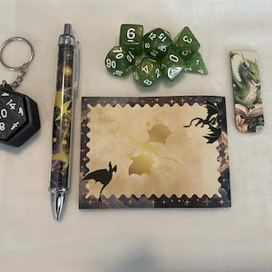 May include: A collection of fantasy-themed items, including a black 20-sided die keychain, a pen with a celestial design, a set of green dice, a bookmark with a dragon, and a decorative card with a dragon illustration.