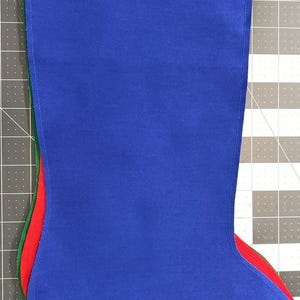 Puede incluir: Una pila de tres calcetines navideños de tela superpuestos. El calcetín superior es azul real, el del medio es rojo brillante y el inferior es verde bosque. Cada calcetín presenta un diseño sencillo y sin adornos adicionales.