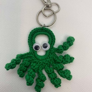 Puede incluir: Llavero de pulpo de crochet verde con ojos saltones y un anillo y cierre de metal plateado.