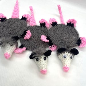 Puede incluir: Tres posavasos de ganchillo con forma de zarigüeya, con orejas rosas, ojos negros y cuerpo gris. Los posavasos están hechos con un hilo suave y tienen un diseño lindo y caprichoso.