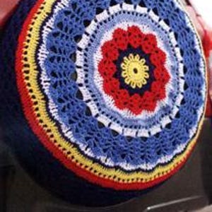 Op de afbeelding: Een kleurrijke gehaakte reservewielhoes met een blauw, geel, rood en wit ontwerp. De hoes heeft een cirkelvormig patroon met een centraal bloemenmotief.