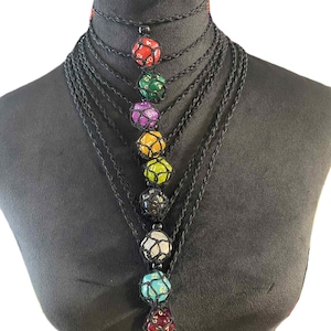 May include: A multi-strand black necklace featuring seven colorful dice pendants. Each die is encased in a net-like structure, with colors including red, green, purple, yellow, black, white, and teal. The necklace is displayed on a black mannequin.
