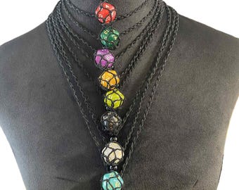 May include: A multi-strand black necklace featuring seven colorful dice pendants. Each die is encased in a net-like structure, with colors including red, green, purple, yellow, black, white, and teal. The necklace is displayed on a black mannequin.