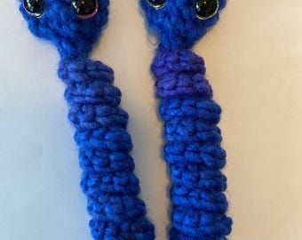 May include: Two blue crocheted worm-like figures with black eyes and a purple band around the middle.