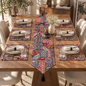 May include: A rectangular table runner and four matching placemats featuring a vibrant patchwork pattern in red, blue, and yellow. The runner includes black tassels at both ends. Each place setting includes a white plate, napkin, and glass.