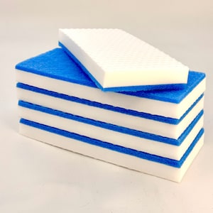 May include: A stack of five white cleaning sponges with blue edges. The sponges are rectangular and have a textured surface.