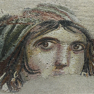 May include: A mosaic artwork depicting a human face. The face is composed of small, colorful tiles in shades of brown, beige, green, and pink. The person has brown eyes and hair, and is wearing a head covering.