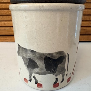 Peut inclure: Un pot en céramique crème avec une illustration de vache noire et blanche. Le pot a un couvercle marron foncé et des accents carrés rouges à la base. Le design est rustique et rappelle la décoration de ferme.