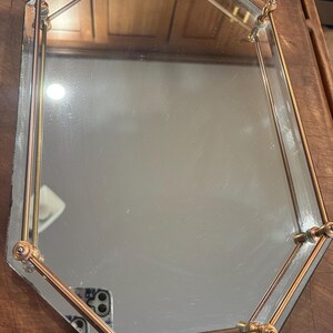 May include: An octagonal mirrored tray featuring a polished brass-toned metal railing around the perimeter. The tray has a reflective glass surface and is supported by small, decorative metal posts at each corner and along the edges.