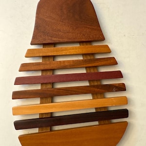 May include: A wooden pear-shaped trivet with a variety of wood tones. The top is a solid, dark brown, while the body is made of horizontal slats in shades of orange, red, and brown. A small, light-colored wooden stem is at the top.