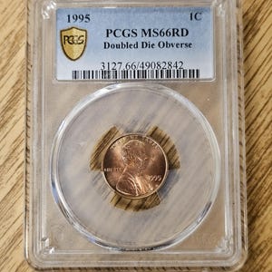 May include: A 1995 PCGS MS66RD Doubled Die Obverse penny encased in a clear plastic holder. The penny is copper-colored and features the profile of a person. The holder has a blue and gold label with the PCGS logo and grading information.