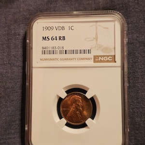 May include: A 1909 VDB 1C MS 64 RB penny encased in a clear plastic holder. The holder has the text "NUMISMATIC GUARANTY COMPANY" and "NGC". The penny is copper-colored and features a portrait and the word "LIBERTY".