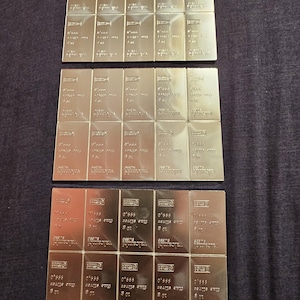 May include: Arrangement of silver bars, each stamped with "999.0 fine silver" and "10 g" or "8 oz" markings. The bars are rectangular with a reflective, metallic finish, and are neatly organized in rows.