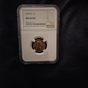 May include: A 1944 S Lincoln wheat penny encapsulated in a clear plastic NGC slab. The label reads 1944 S 1C MS 66 RD with the serial number 8696959-012. The copper coin features the profile of Abraham Lincoln facing right on the obverse side.
