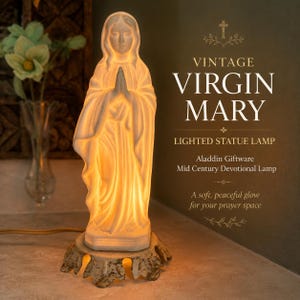 May include: A white ceramic Virgin Mary statue lamp emitting a warm internal glow. The figure stands with hands clasped in prayer on a decorative, scalloped metal base. Text on the image reads: VINTAGE VIRGIN MARY LIGHTED STATUE LAMP Aladdin Giftware.