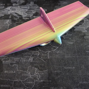 May include: A 3D printed iridescent pink and yellow airplane wing with a textured surface.