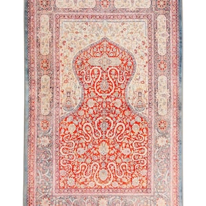 May include: A rectangular rug with an intricate floral design in red, cream, and blue. The central field is dominated by a red pattern, with a cream-colored arch shape at the top. The rug has a blue border and gray tassels.