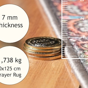 May include: A prayer rug with a colourful floral pattern, measuring 80x125 cm and weighing 1,738 kg. The rug is 7 mm thick and is shown next to a ruler and a stack of coins.