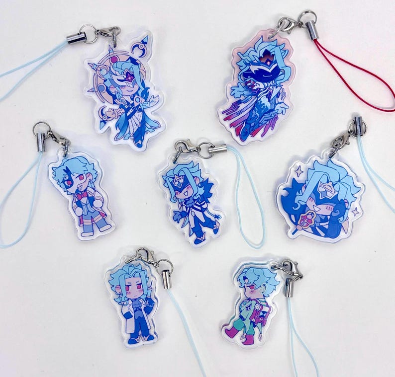 May include: A collection of seven acrylic charms featuring anime-style characters in shades of blue, white, and pink. Each charm has a silver clasp and a light blue lanyard. The characters have various poses and outfits.